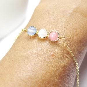 May include: A gold chain bracelet with three round gemstone beads. The beads are light blue, white, and pink.
