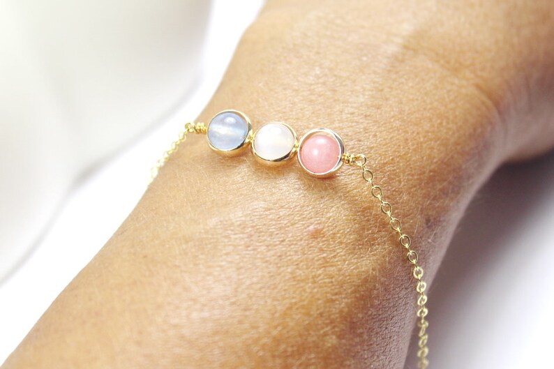 May include: A gold chain bracelet with three round gemstone beads. The beads are light blue, white, and pink.