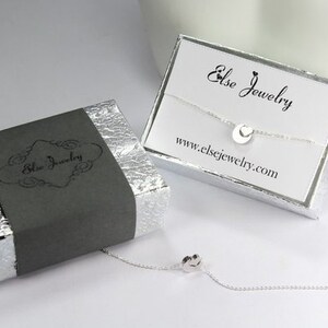 K&ouml;nnte beinhalten: Eine silberne Halskette mit einem kleinen runden Anh&auml;nger, verpackt in einer grauen Schachtel mit dem Text "Else Jewelry" und einer wei&szlig;en Schachtel mit dem Text "Else Jewelry" und der Website-Adresse "www.elsejewelry.com".