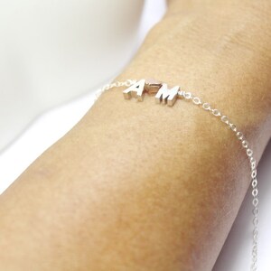 May include: A silver chain bracelet with the letters "AM" hanging from it.