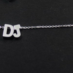 May include: A silver chain necklace with a pendant that says "DJ" in block letters.