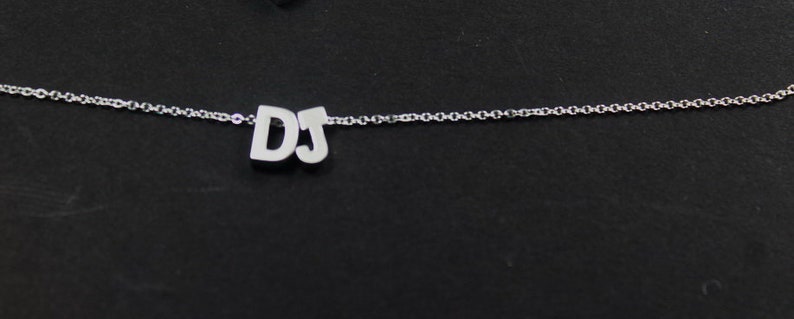 May include: A silver chain necklace with a pendant that says "DJ" in block letters.