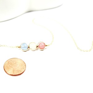 May include: A gold chain necklace with three beads: light blue, white, and pink. The necklace is about the size of a UK penny.