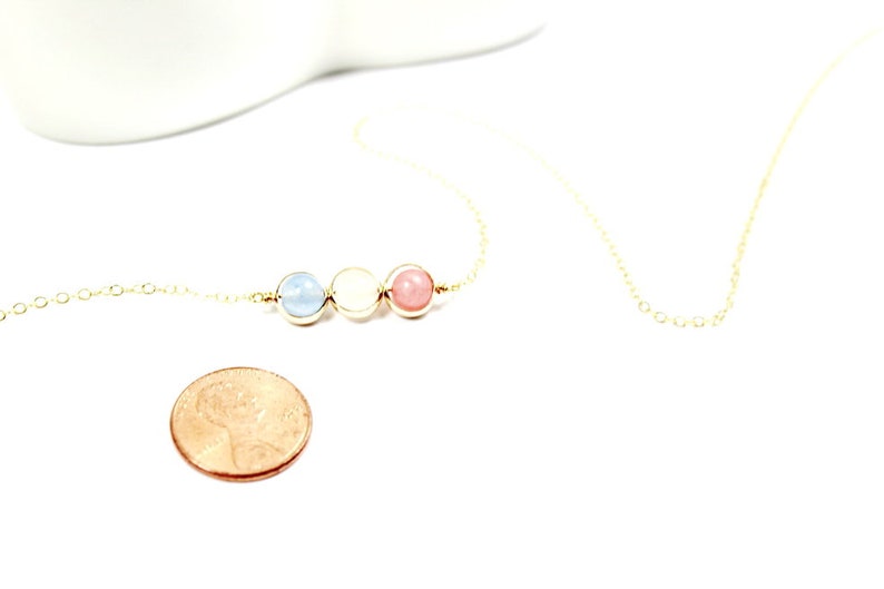May include: A gold chain necklace with three beads: light blue, white, and pink. The necklace is about the size of a UK penny.