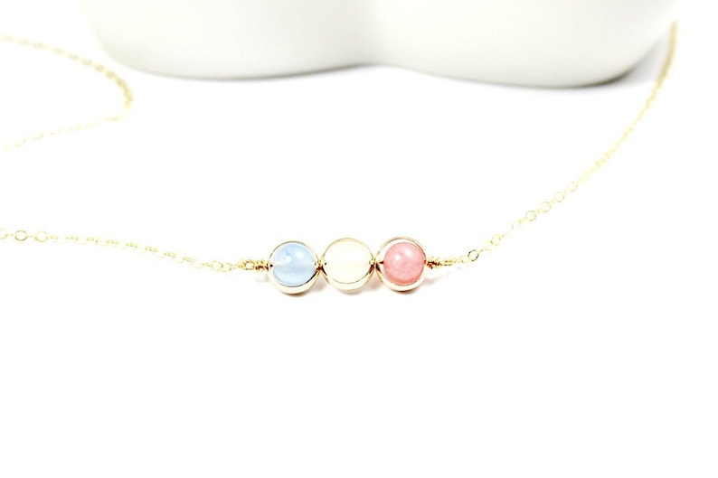 May include: A gold chain necklace with three round beads. The beads are light blue, white, and pink.
