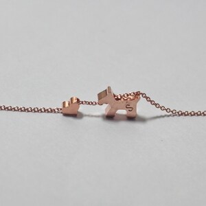 May include: A rose gold necklace with a small heart charm and a larger charm shaped like a dog. The dog charm has the letter "S" engraved on it.