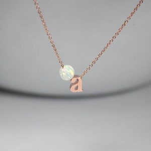 May include: A rose gold necklace featuring a small opal bead and a letter 'a' charm.