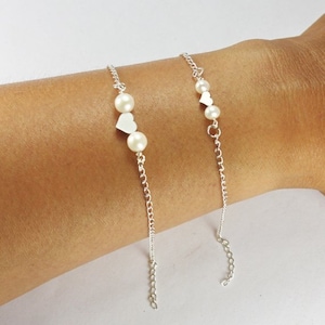 K&ouml;nnte beinhalten: Zwei silberne Kettenarmb&auml;nder mit kleinen wei&szlig;en Perlen und silbernen Herzanh&auml;ngern.