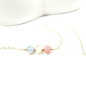 May include: A gold chain necklace with three beads: a light blue bead, a white bead, and a pink bead.
