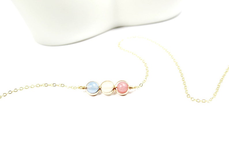 May include: A gold chain necklace with three beads: a light blue bead, a white bead, and a pink bead.
