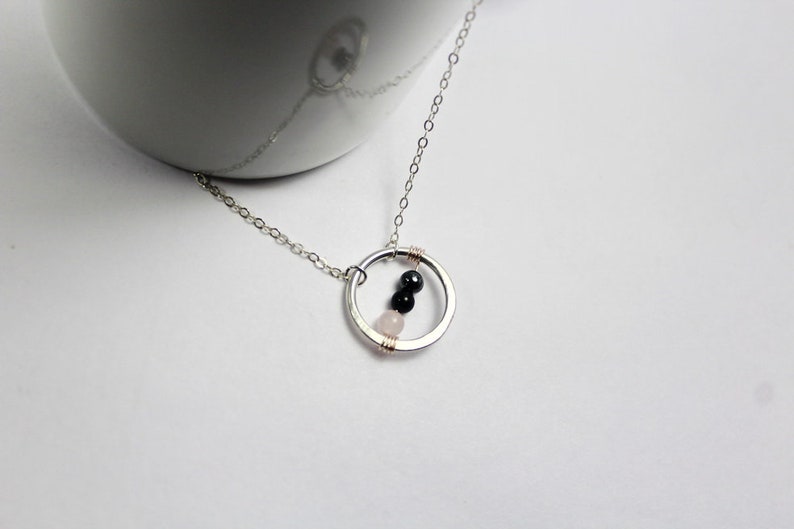 May include: A silver necklace with a circle pendant featuring three beads: two black and one pink.
