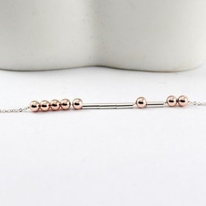 Pu&ograve; includere: Un braccialetto delicato con catena d'argento con perline e distanziatori in oro rosa. Il braccialetto presenta un design semplice con una fila di perline e distanziatori.