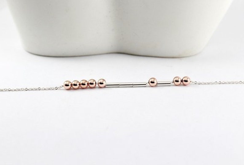 Pu&ograve; includere: Un braccialetto delicato con catena d'argento con perline e distanziatori in oro rosa. Il braccialetto presenta un design semplice con una fila di perline e distanziatori.