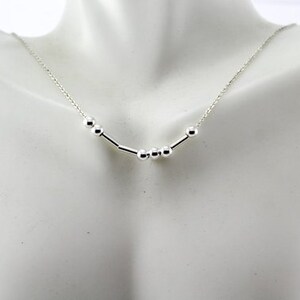 Pu&ograve; includere: Una collana d'argento con una catena delicata e un design semplice con piccole perle rotonde e barre di collegamento.