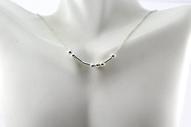 Pu&ograve; includere: Una collana d'argento con una catena delicata e un design semplice con piccole perle rotonde e barre di collegamento.