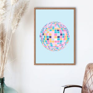 May include: A framed print of a colourful disco ball on a light blue background. The disco ball is made up of many small squares in shades of pink, blue, yellow, and purple.
