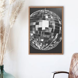 May include: A black and white photograph of a disco ball hanging from the ceiling. The disco ball is made of many small mirrors that reflect light.