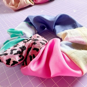 Op de afbeelding: Een kleurrijke haarband gemaakt van verschillende stoffen met patronen, waaronder roze luipaardprint, blauw-witte tie-dye en groen-witte bloemenprint.
