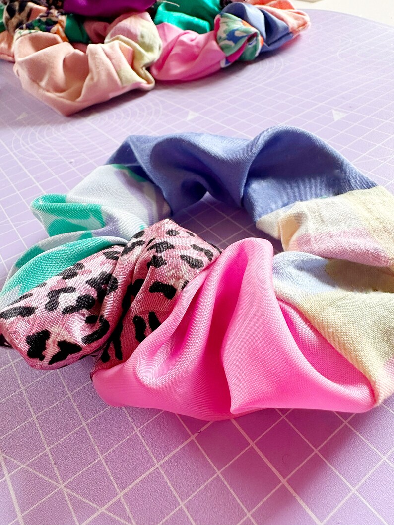 Op de afbeelding: Een kleurrijke haarband gemaakt van verschillende stoffen met patronen, waaronder roze luipaardprint, blauw-witte tie-dye en groen-witte bloemenprint.