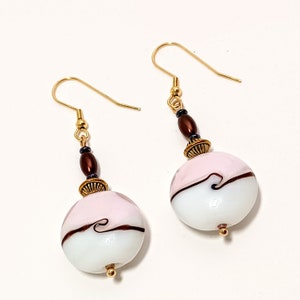 May include: A pair of gold dangle earrings with pink and white glass beads. The beads have a swirl design and are accented with brown and gold beads.