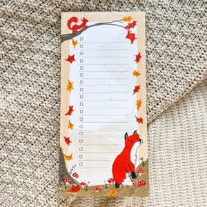 May include: A wooden notepad with an autumn theme. The notepad has a checklist with a squirrel and a fox on it. The background is a wood grain pattern with red and yellow leaves.