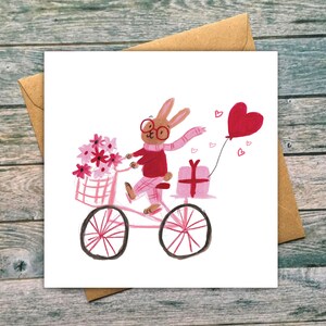 May include: A pink bicycle with a basket of pink flowers, a pink gift box, and a red heart balloon. A brown rabbit with red glasses and a pink scarf is riding the bicycle.