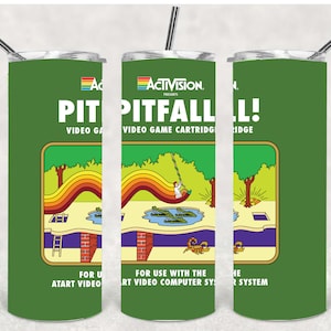 May include: Green tumbler featuring the classic Atari video game, Pitfall!. The design includes the game's logo and a colorful graphic of the game's landscape. The tumbler has a silver straw and a white lid.