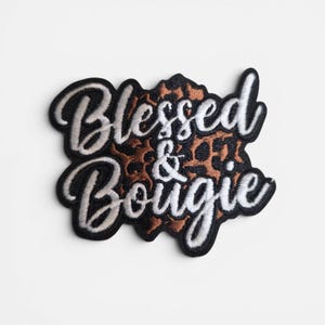 May include: Embroidered patch with the words "Blessed & Bougie" in white script lettering, outlined in black. The center features a leopard print design in shades of brown and tan. The patch has a black border.