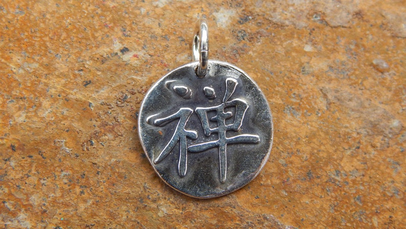 May include: Silver pendant with the Chinese character for "Zen" embossed on it.