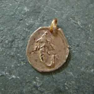 May include: A bronze-colored pendant with a detailed fly fishing lure design. The pendant has a small loop at the top for a chain. The pendant is approximately 1 inch in diameter.