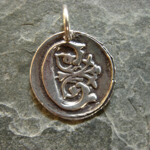 May include: A silver pendant with a decorative letter G in a circular design.