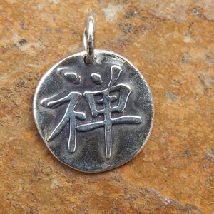 May include: Silver pendant with the Chinese character for Zen, "Zen", embossed on a round disc.
