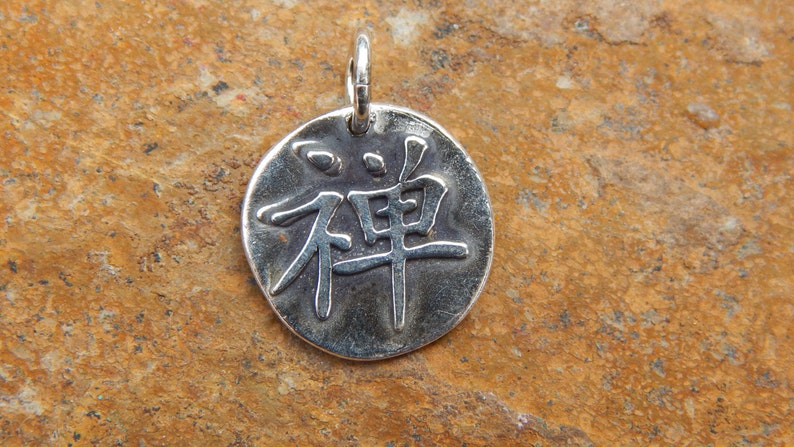 May include: Silver pendant with the Chinese character for Zen, "Zen", embossed on a round disc.