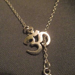 May include: Silver-toned necklace featuring the Om symbol pendant. The pendant is a stylized representation of the sacred sound. The necklace has a delicate chain and a small extension chain.