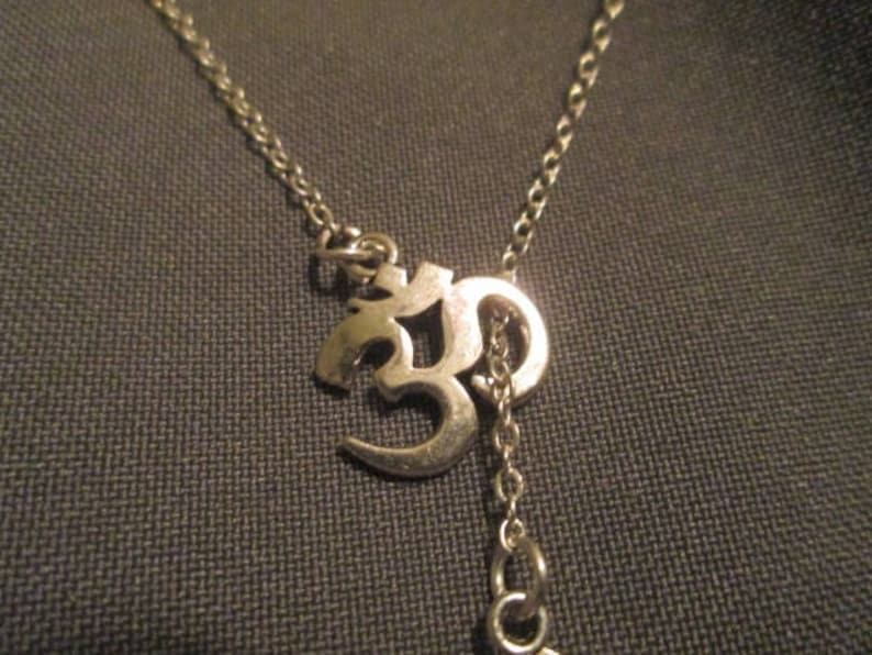 May include: Silver-toned necklace featuring the Om symbol pendant. The pendant is a stylized representation of the sacred sound. The necklace has a delicate chain and a small extension chain.