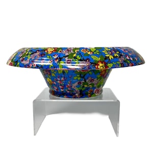 May include: A blue floral bowl with a wide, flat rim. The bowl is decorated with colourful flowers and foliage. It is displayed on a clear acrylic stand, showcasing its decorative design.
