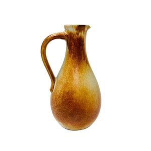 May include: A ceramic pitcher with a rounded body and a single curved handle. The surface features a blended glaze with warm tones of amber, golden yellow, and cream, transitioning from a darker, saturated base to a lighter, muted upper neck.