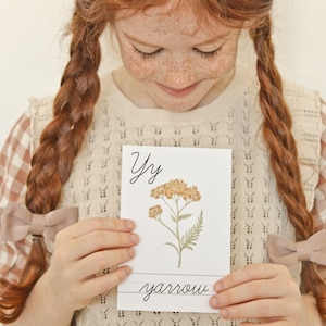 Pu&ograve; includere: Un cartoncino bianco con la lettera Y e la parola "yarrow" scritta in corsivo. Un'illustrazione ad acquerello di una pianta di achillea con fiori gialli &egrave; sul cartoncino.