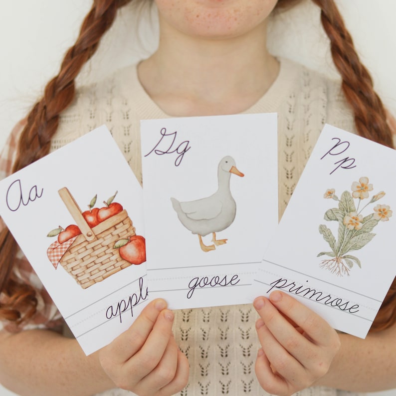 Pu&ograve; includere: Tre flashcard con lettere scritte a mano e illustrazioni. La prima carta mostra la lettera 'Aa' e un cesto di mele rosse. La seconda carta mostra la lettera 'Gg' e un'oca bianca. La terza carta mostra la lettera 'Pp' e una primula gialla.