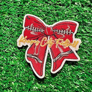 May include: Red fabric bow with white stitching and a gold embroidered "Kansas City Football" text.