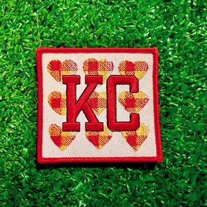 May include: Red and white checkered heart patch with the letters "KC" in red.