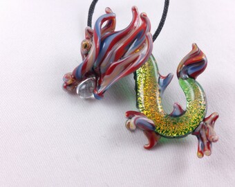 May include: A glass dragon pendant with red, white and blue swirls on the head and tail, and a green body with gold glitter. The pendant is on a black cord.