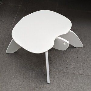 May include: White, modern, minimalist, child-sized stool with a unique, organic, curved design. The stool is made of a lightweight material and has a smooth, white finish.