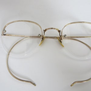 May include: Gold-tone rimless eyeglasses with a delicate wire frame and clear lenses. The glasses have a classic, vintage style.