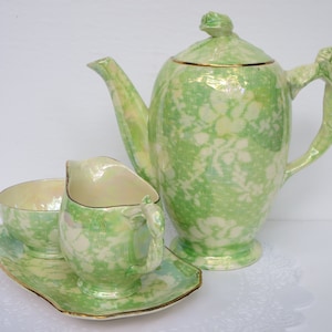 May include: A green and white tea set with a teapot, creamer, sugar bowl, and a matching tray. The set has a floral pattern and a pearlescent finish.