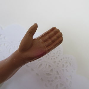 May include: Close-up of a brown, sculpted hand with fingers outstretched, appearing to be part of a figurine.