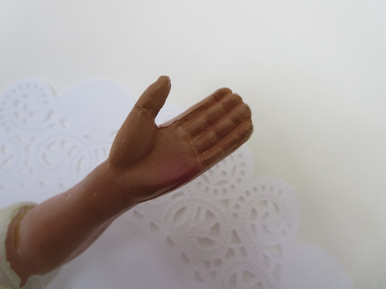 May include: Close-up of a brown, sculpted hand with fingers outstretched, appearing to be part of a figurine.