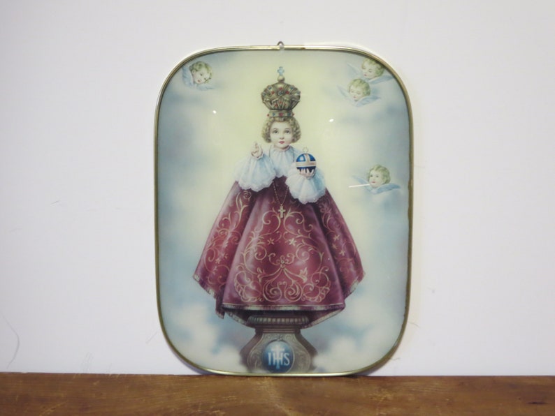 Peut inclure: Une image encadr&eacute;e d'une figure religieuse, un jeune gar&ccedil;on portant une couronne et une robe rouge, tenant un globe. L'image est entour&eacute;e d'anges et porte le mot "THIS" en bas.