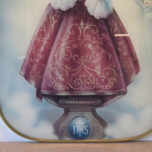 Peut inclure: Une image encadr&eacute;e d'une figure religieuse, une jeune fille portant une robe rouge et or avec une couronne et un collier avec une croix. L'image est sur un fond blanc avec un cadre dor&eacute;.