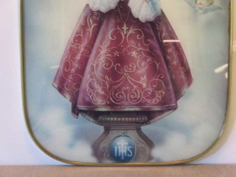 Peut inclure: Une image encadr&eacute;e d'une figure religieuse, une jeune fille portant une robe rouge et or avec une couronne et un collier avec une croix. L'image est sur un fond blanc avec un cadre dor&eacute;.